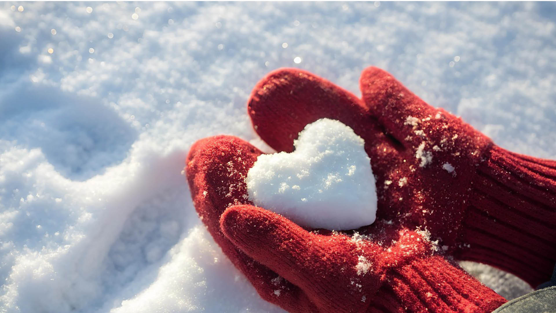 Två röda stickade vantar håller en hjärta av snö