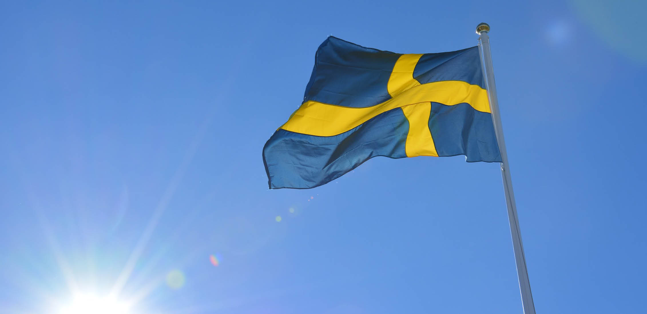 Bild på svenska flaggan mot klarblå himmel